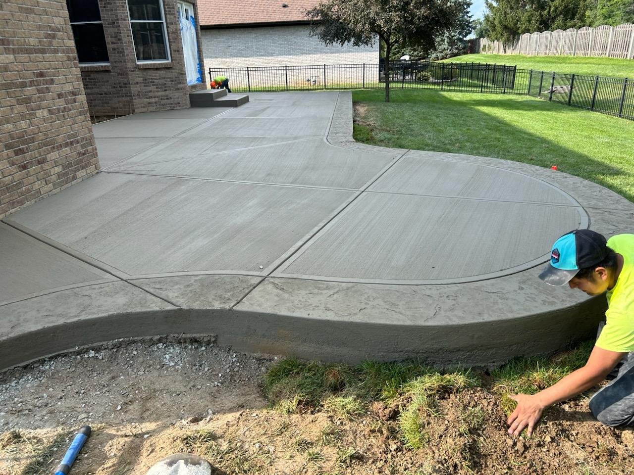 Curved broom-finished concrete patio beside backyard landscaping