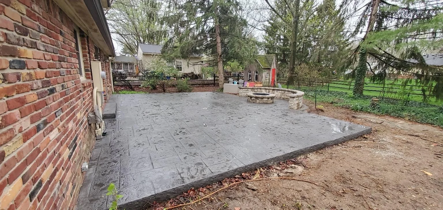 Dark gray stamped concrete patio beside a brick home